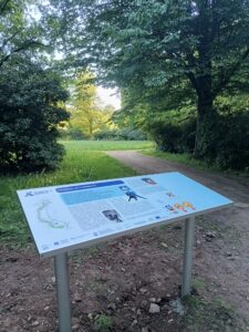 Informationstafel vor einer Wiese mit Bäumen